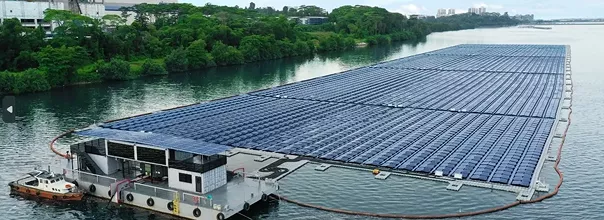 a large floating solar farm spread across a body of water, arranged in a precise grid pattern. a small structure, likely a control or maintenance facility, is situated on the left, with surrounding greenery