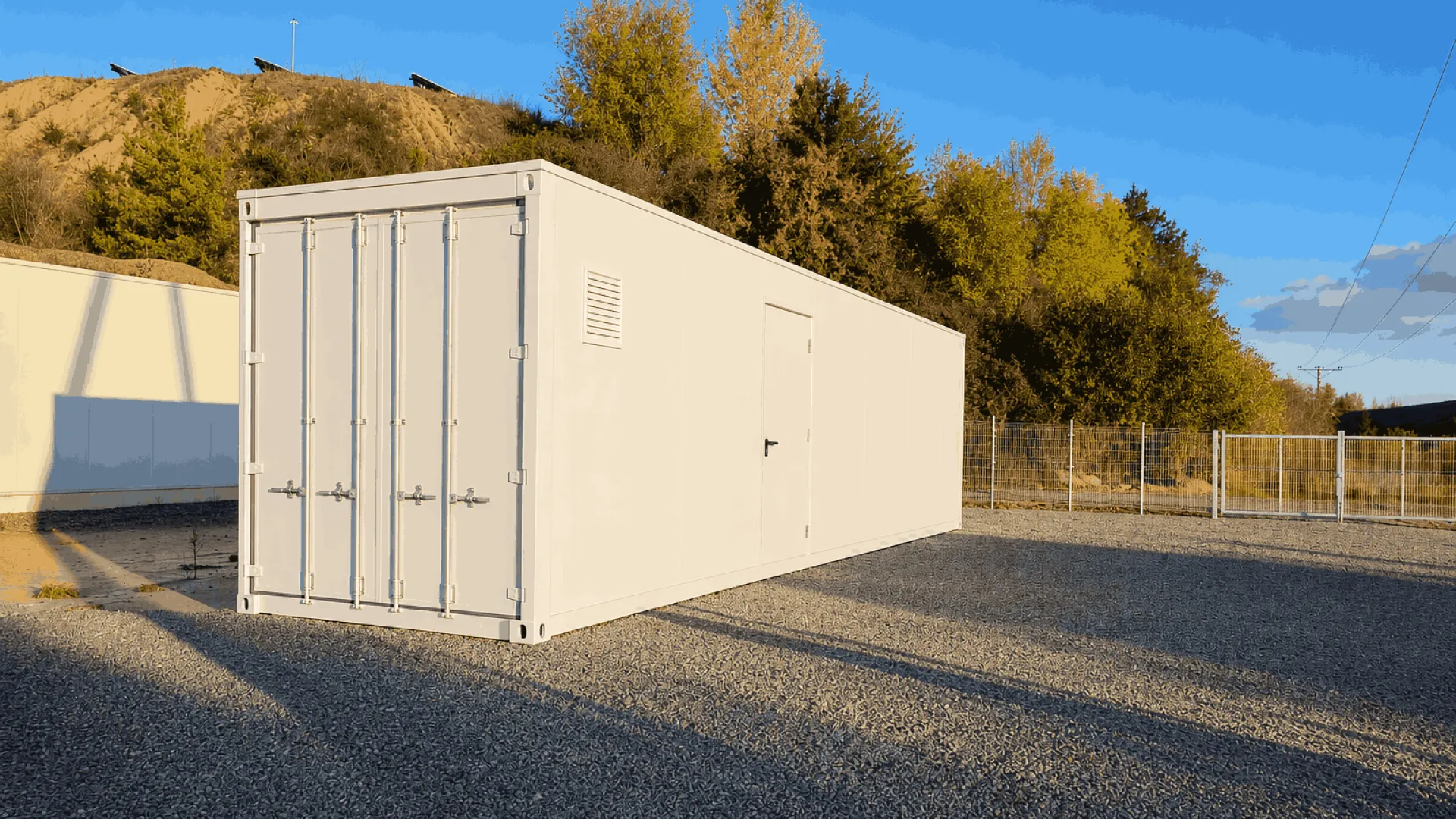 White storage container on gravel lot at sunset, trees and hill in background