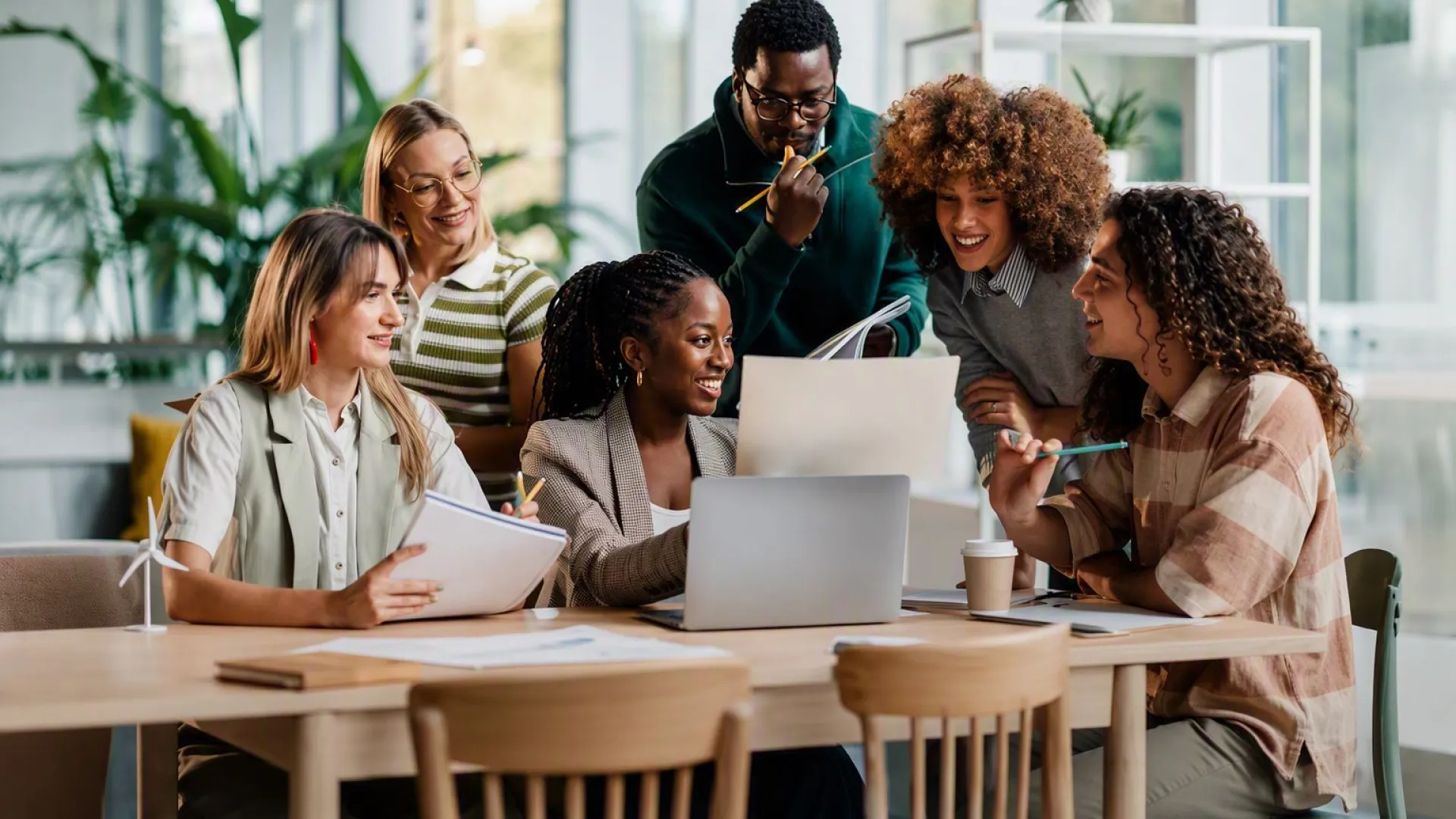 A group of people gathered around a laptop in a modern office, collaborating on a project and reviewing documents together.