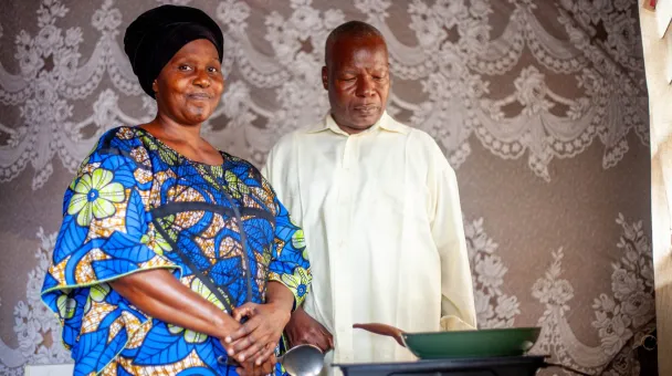 A couple posing in front of an electric stove with a fridge on top of it