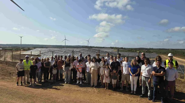 Group of people posing for a picture in front of a solar installation park and some windmills 