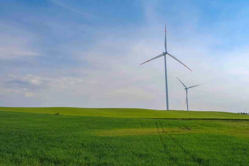 Two wind turbines on rolling green fields under a bright blue sky.