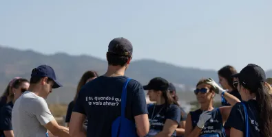 group of employees gathered on the beach with one employee's back facing the camera wearing an official volunteering t shirt 
