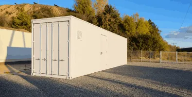 White storage container on gravel lot at sunset, trees and hill in background