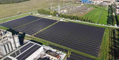 Aerial view of large solar panel fields beside industrial buildings and green farmland
