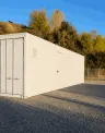 White storage container on gravel lot at sunset, trees and hill in background