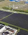 Aerial view of large solar panel fields beside industrial buildings and green farmland